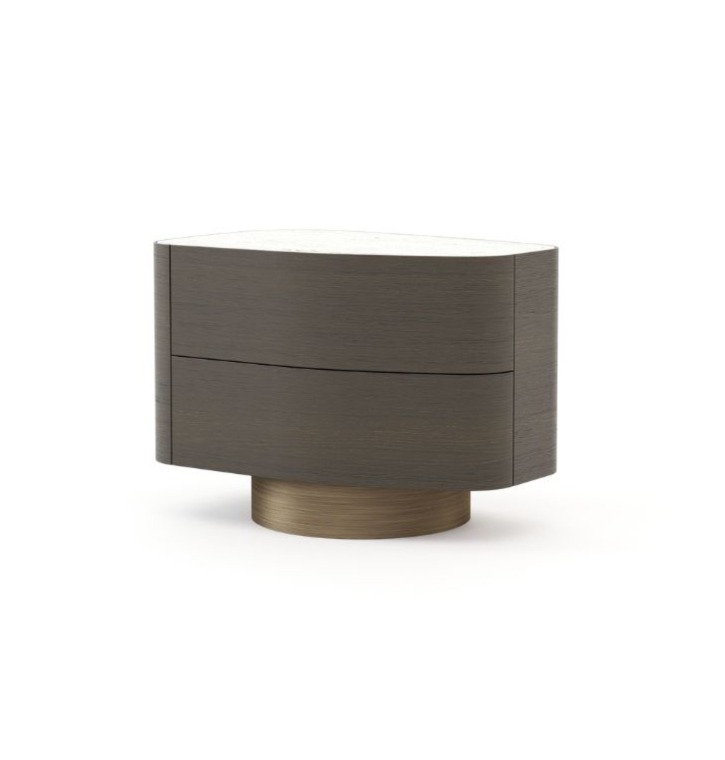 Il tavolino Stone, realizzato in legno scuro con due cassetti arrotondati e un piano in pietra bianca liscia, poggia su una base circolare in bronzo spazzolato ed è presentato in un ambiente minimalista che ne esalta la silhouette ovale.