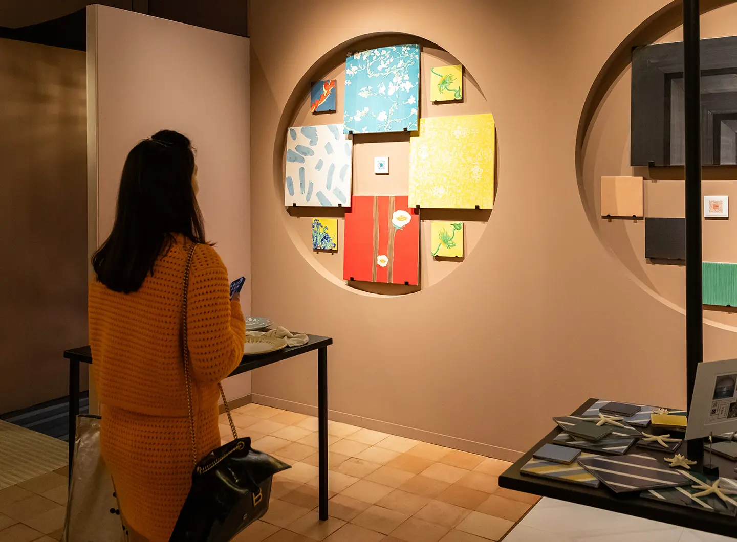 Donna di spalle che guarda delle composizioni di maioliche quadrate appese al muro