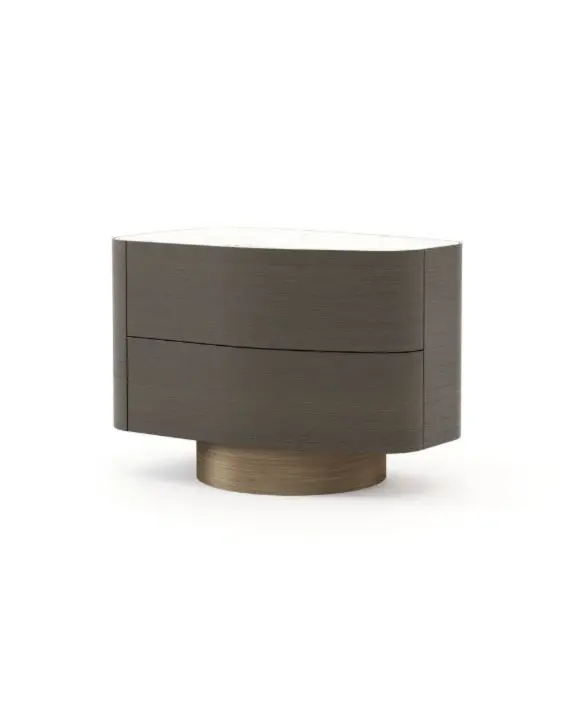 Il tavolino Stone, realizzato in legno scuro con due cassetti arrotondati e un piano in pietra bianca liscia, poggia su una base circolare in bronzo spazzolato ed è presentato in un ambiente minimalista che ne esalta la silhouette ovale.