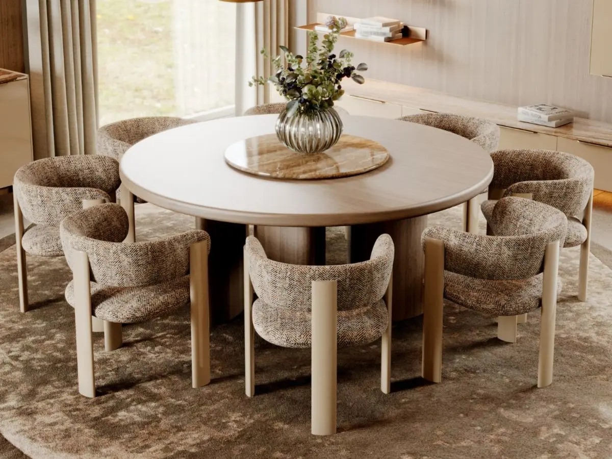Il Tavolo da pranzo Rotondo Dolomites è mostrato in una sala da pranzo elegante con sei sedie imbottite in tessuto disposte attorno, su un tappeto morbido e decorato. Un centrotavola floreale completa la composizione, insieme a tende beige, mensole in legno integrate e un’atmosfera contemporanea e accogliente.